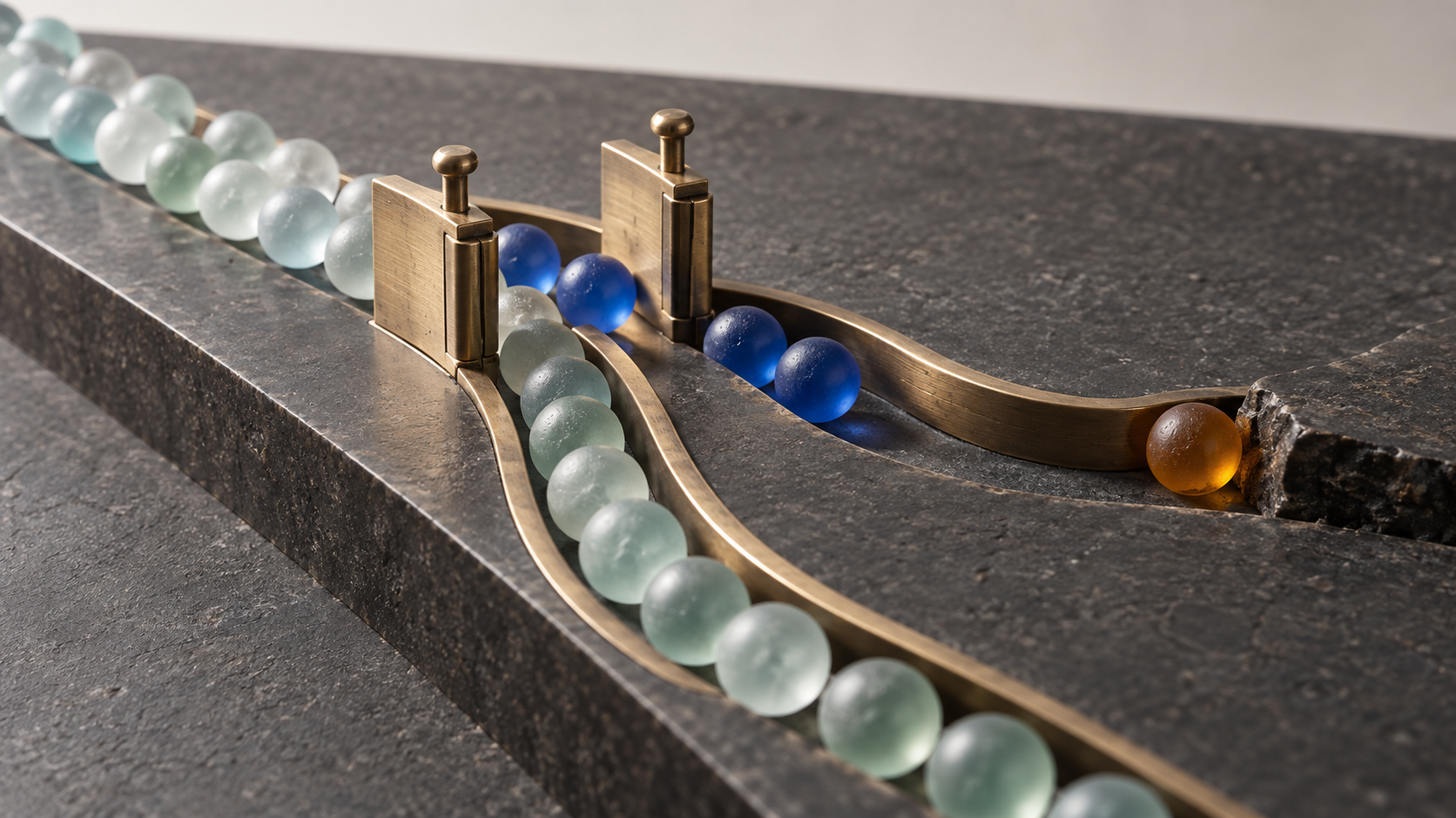 Macro studio still life of frosted glass spheres divided by brass gates, with cobalt spheres on one route and an amber sphere caught at a dark stone edge.